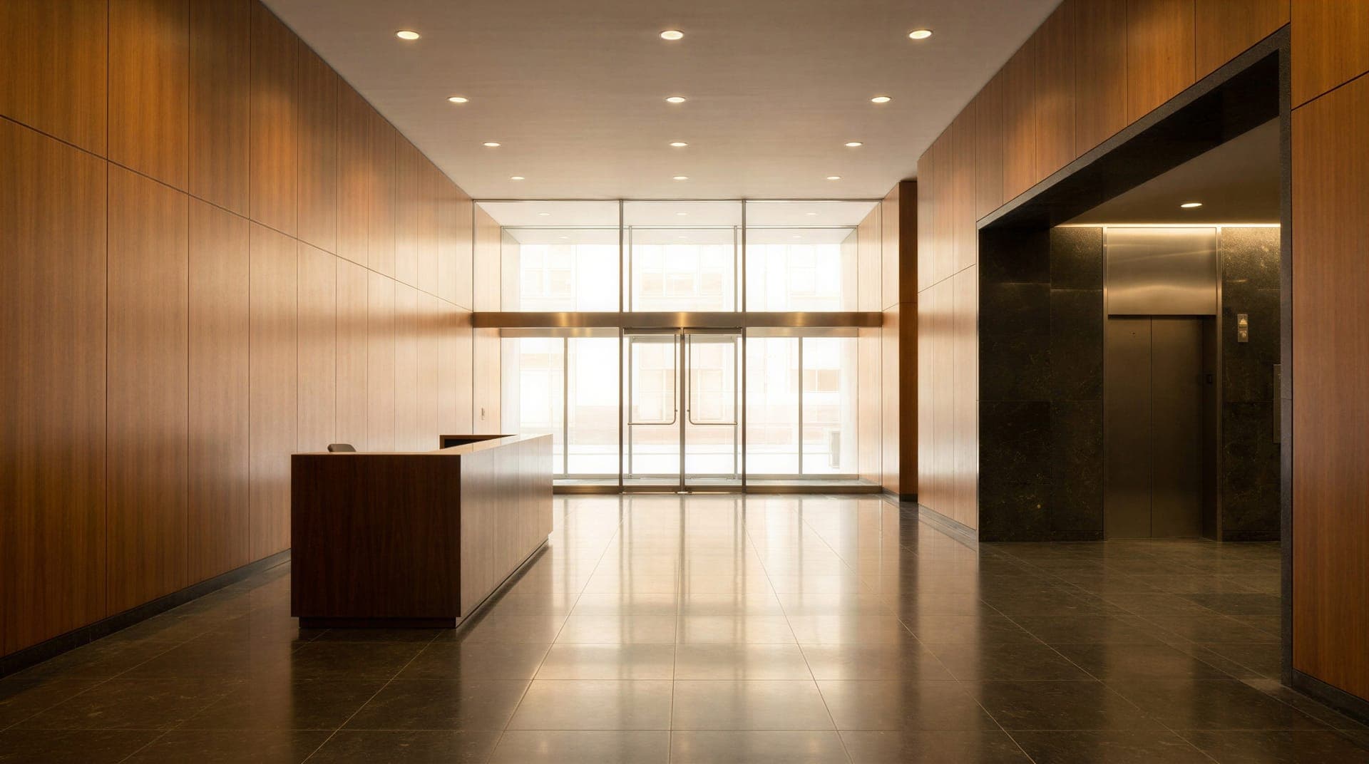 A building lobby with wood-panelled walls, a reception desk, a dark polished stone floor and glass entrance doors